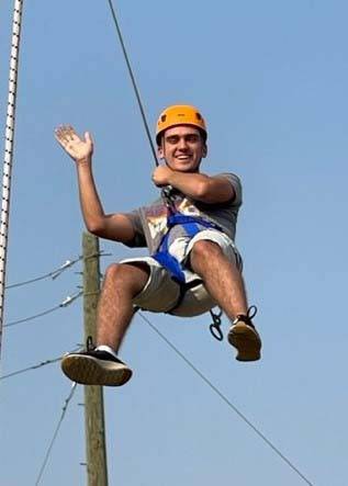 A teen dangles from a safety harness at an adventure course.