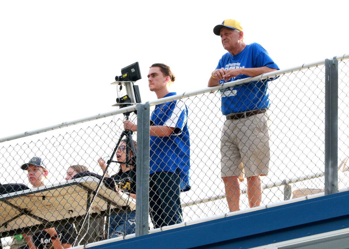 A teenager runs a video camera at a football game.